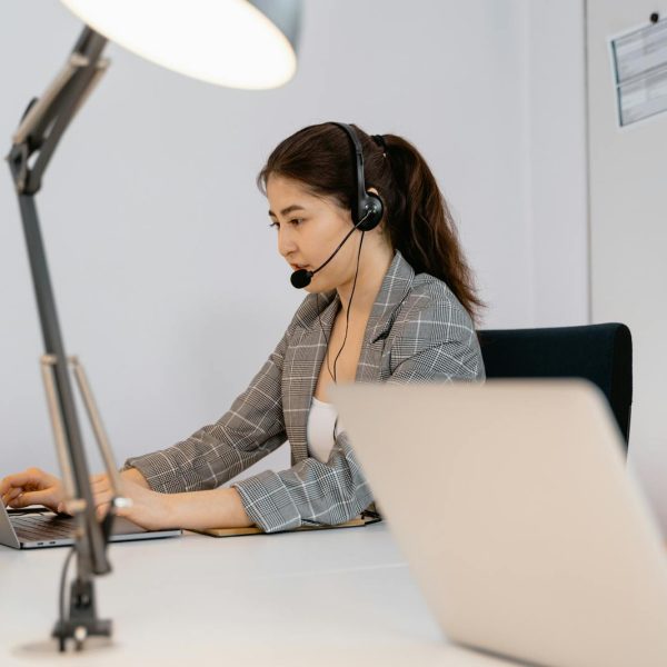 Focused woman at a desk with a headset, providing customer support in an office setting.